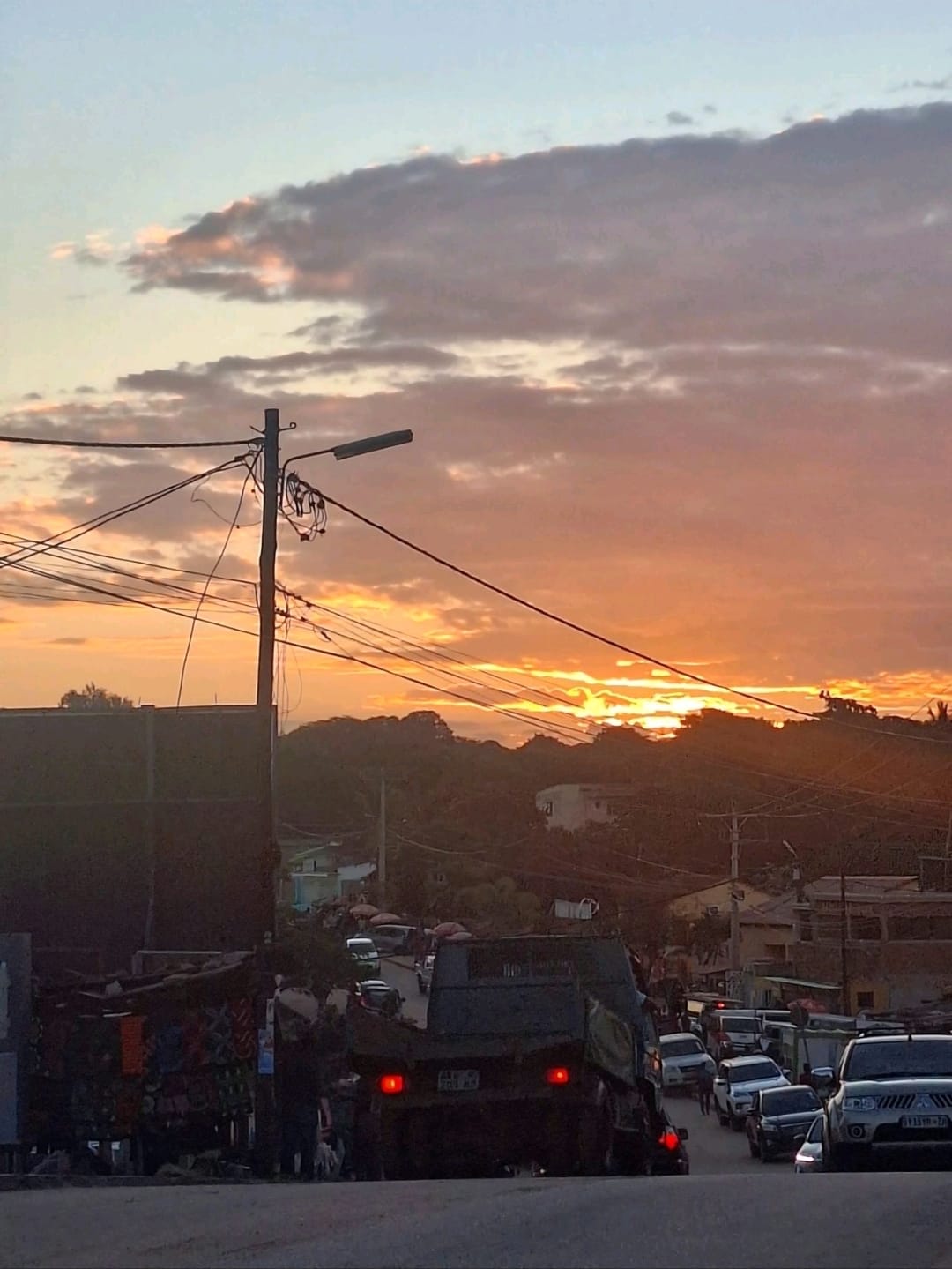 A golden sunset over a busy Maputo street with traffic and roadside stalls