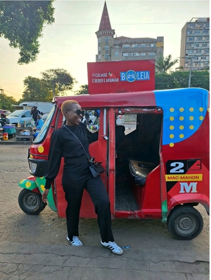 Eunice laughing beside a red and blue tuk-tuk on a Maputo street